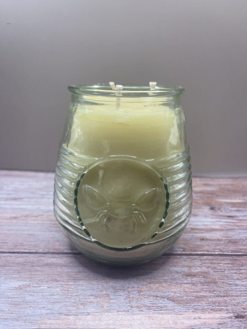 A candle in a glass jar with a lemon slice on the side.